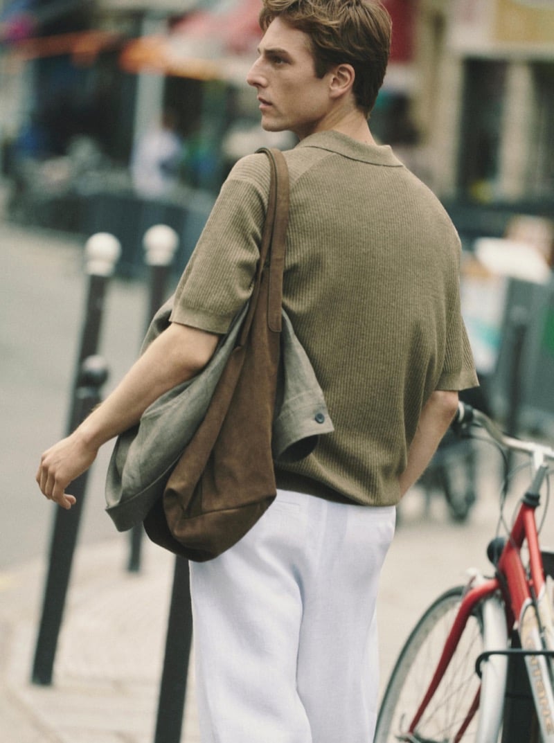 Quentin Demeester from behind in a Massimo Dutti ribbed knit polo and wide linen trousers, a slouchy suede hobo bag riding at the hip