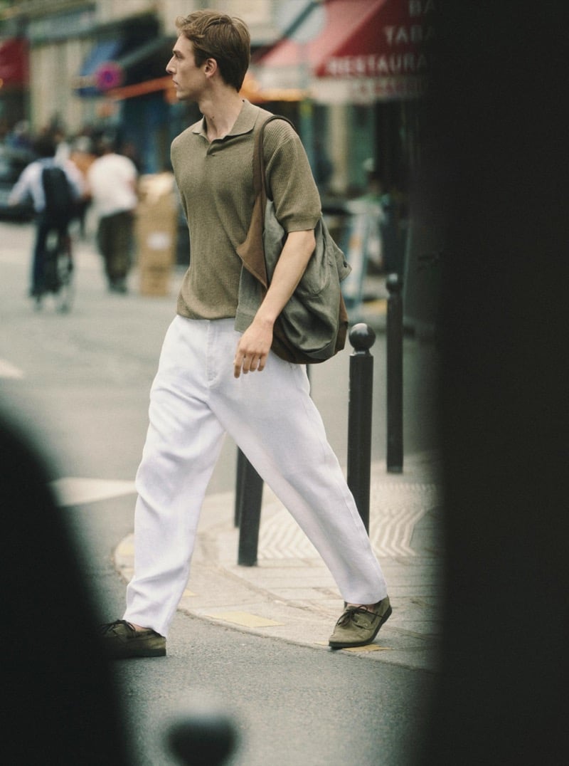 Quentin Demeester crossing a Paris street in a Massimo Dutti ribbed knit polo, wide linen trousers, suede shoulder bag, and moccasins