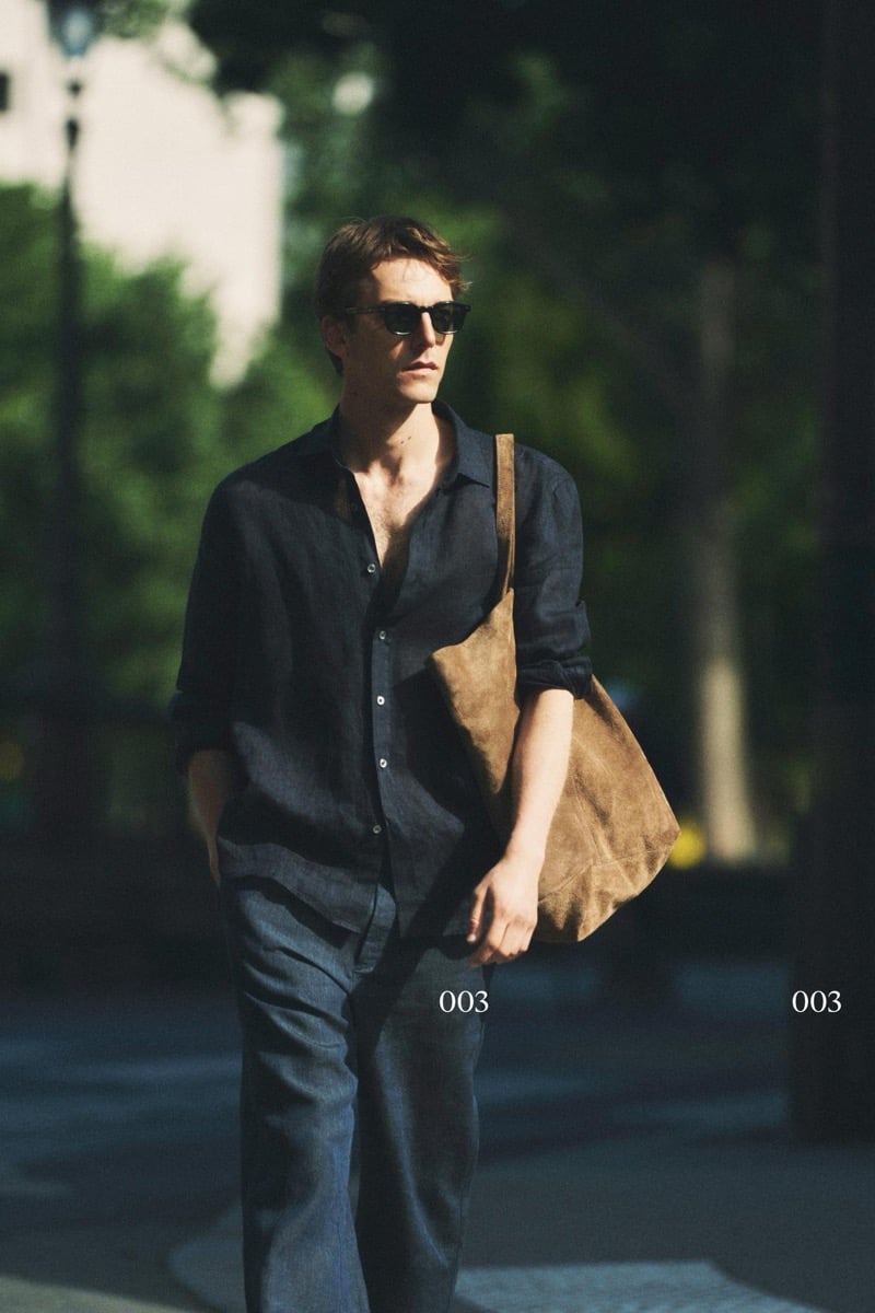Quentin Demeester walking in a Massimo Dutti open linen shirt and trousers with rectangular sunglasses and a slouchy suede tote on the shoulder