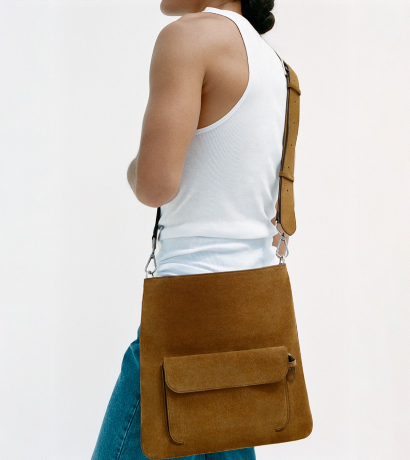 Back view of a figure in a white ribbed cotton tank and faded blue jeans, the Métier Slide Messenger in tobacco Marrakech suede worn crossbody with its adjustable strap angled across the back