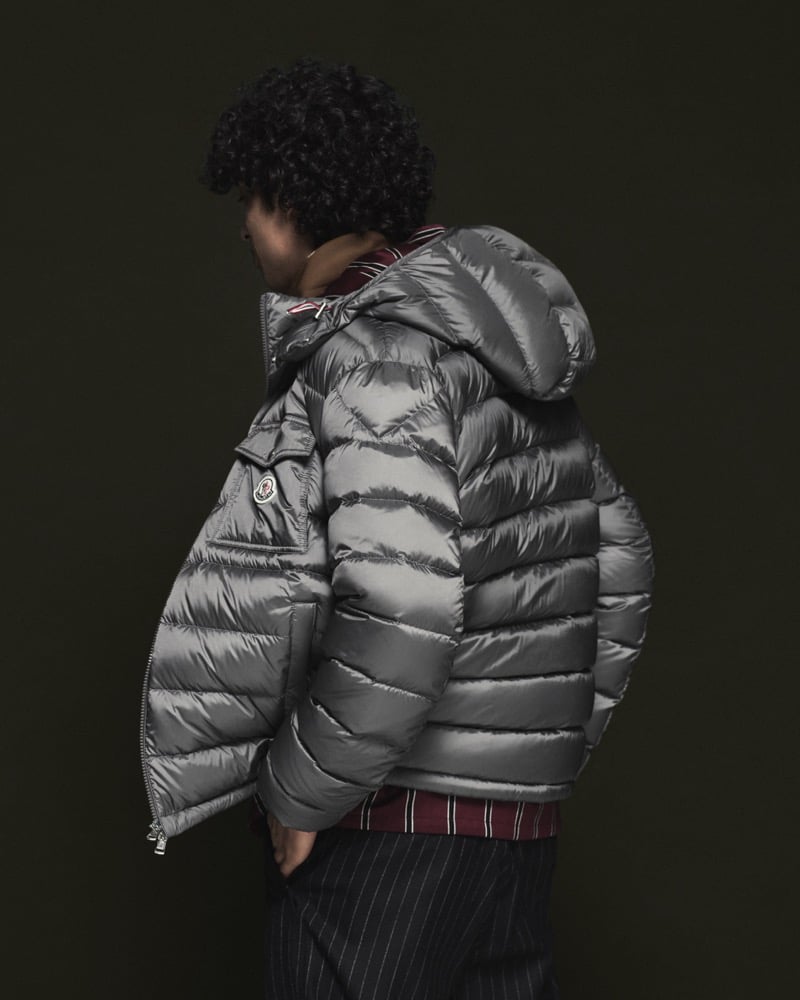 Model Nour Boudaakat in a silver-gray hooded down puffer jacket layered over a burgundy striped shirt with a red, white, and navy placket, paired with charcoal pinstripe trousers