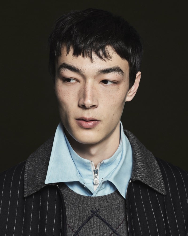 Model Pascal Thulin in a charcoal pinstripe overcoat layered over a gray wool herringbone zip jacket, gray argyle crewneck sweater, and pale blue oxford shirt
