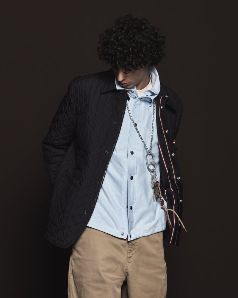 Model Nour Boudaakat in a black diamond-quilted shirt jacket over a pale blue oxford button-down, paired with khaki corduroy trousers and a silver carabiner key chain with charms