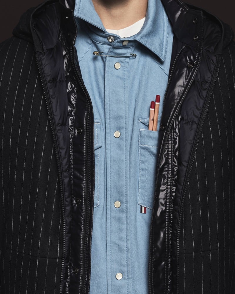 Close-up of a black pinstripe wool coat with a quilted down liner over a chambray blue shirt with pencils tucked in the chest pocket
