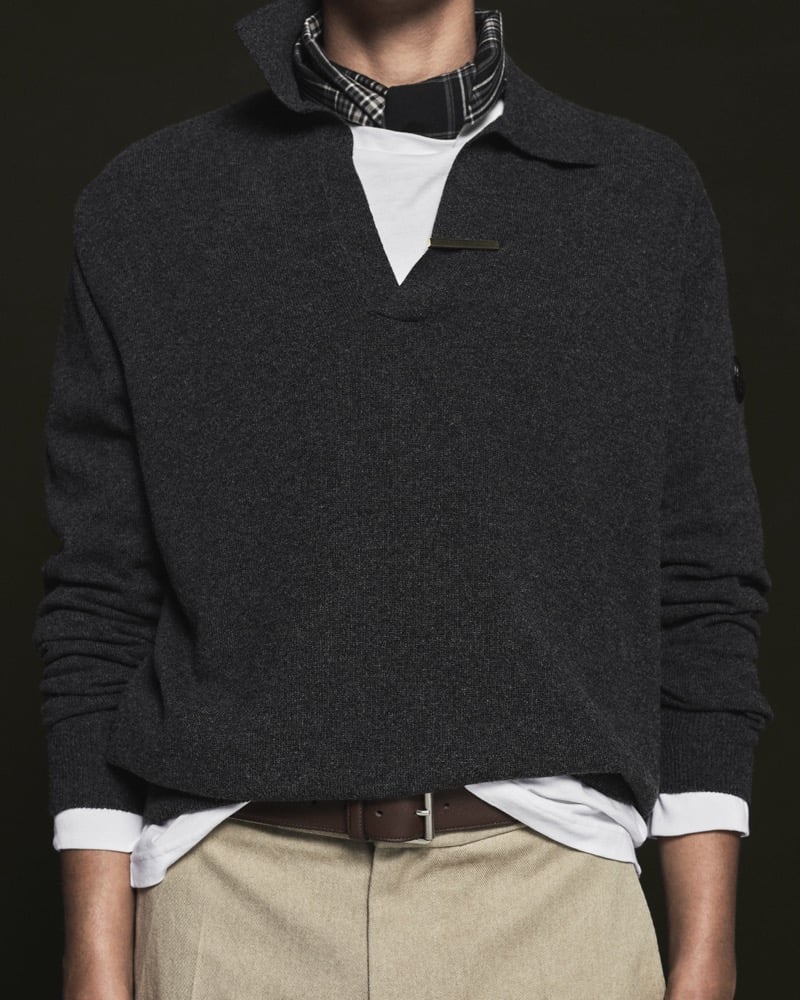 Model Nour Boudaakat in a charcoal cashmere sweater over a white tee, paired with a brown leather belt and stone trousers