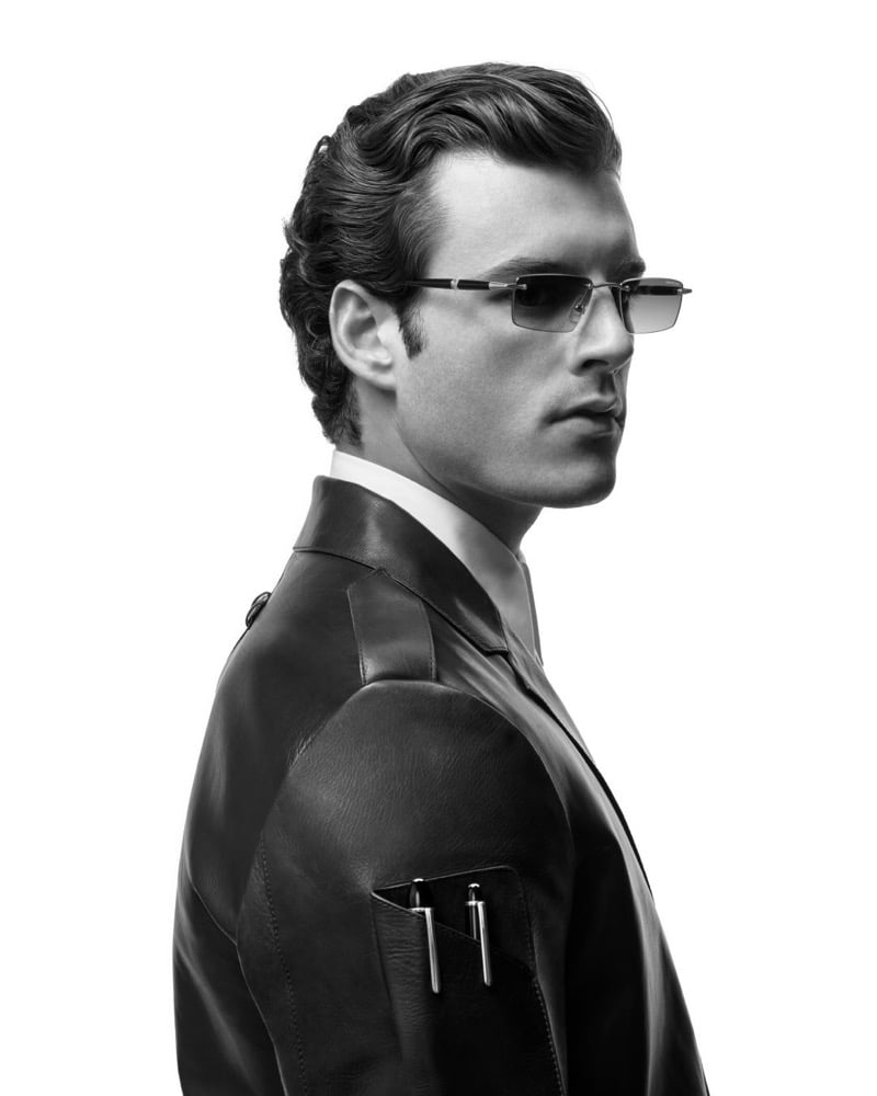Aiden Stonehouse seen in profile wearing semi-rimless sunglasses with metal temples and a leather jacket displaying two Montblanc pens clipped to its sleeve pocket in a black-and-white portrait