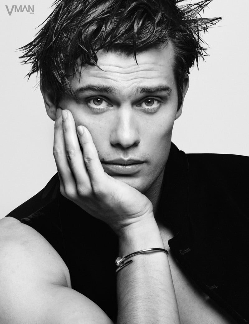 Nicholas Galitzine rests his cheek against his hand in a black Giorgio Armani vest with a silver Cartier bracelet on his wrist