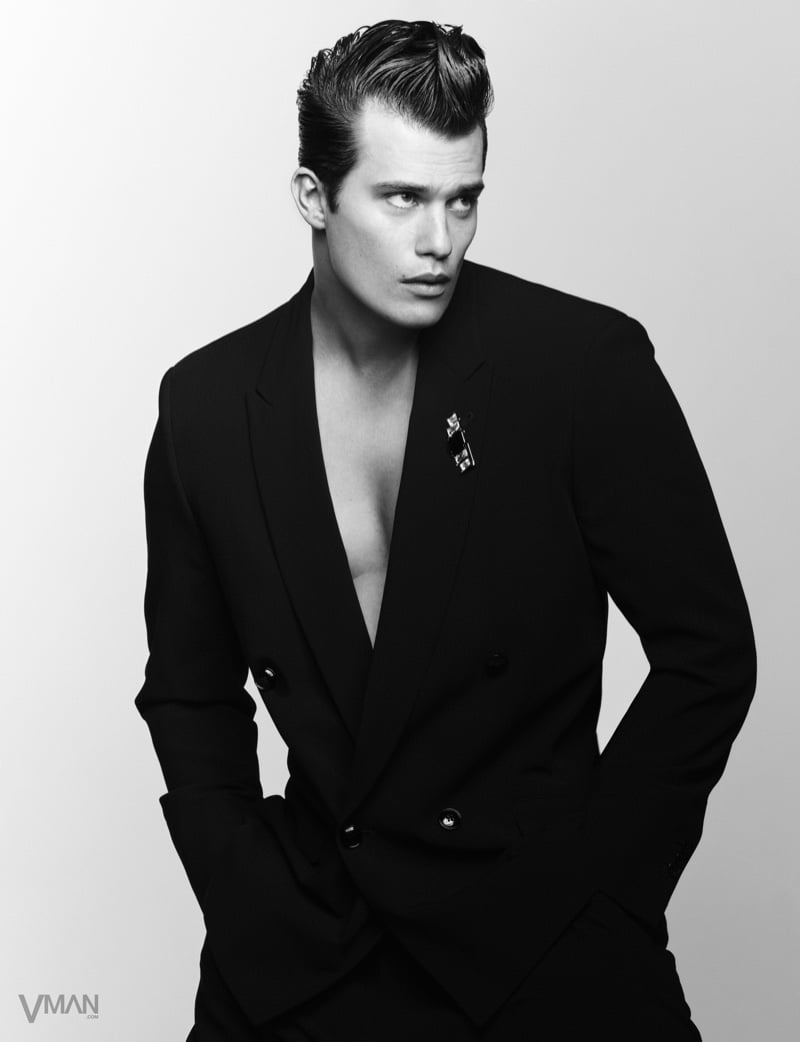 Nicholas Galitzine stands with his hands in his pockets in a black double-breasted Giorgio Armani suit worn open with a brooch on the lapel