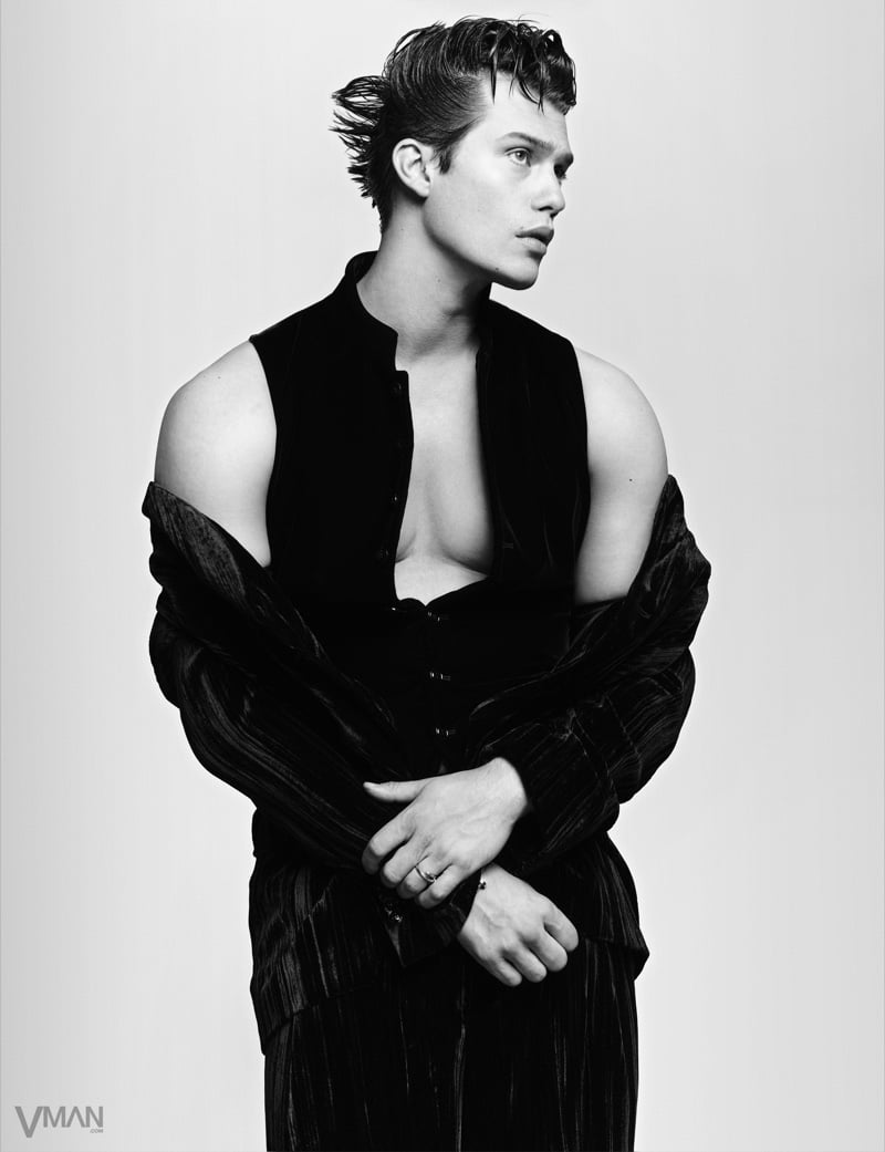 Nicholas Galitzine crosses his arms in a black Giorgio Armani vest layered under a velvet suit pulled off the shoulders, finished with Cartier jewelry