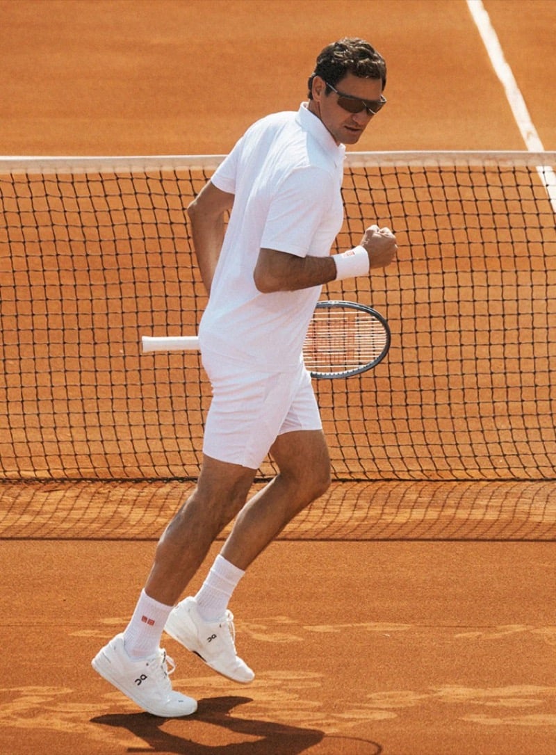 Roger Federer celebrating a point in an all-white tennis kit on the red clay of the Foro Italico, racquet at his side, wearing wrapped shield Oliver Peoples sunglasses