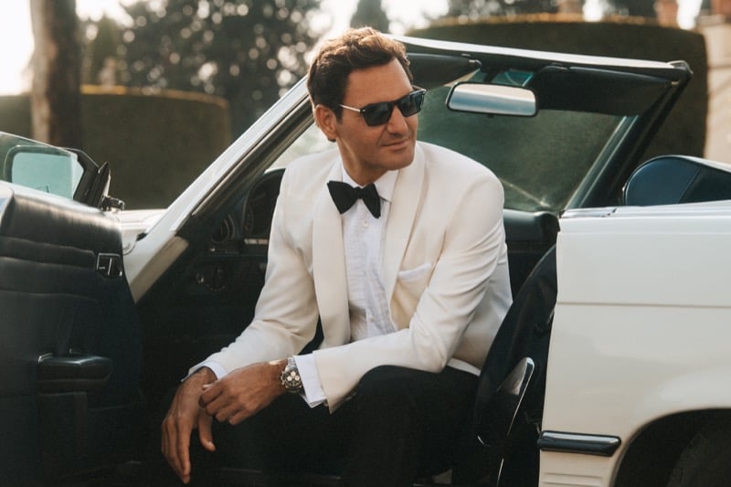 Roger Federer stepping out of a vintage white convertible at a Roman villa in a white shawl-lapel dinner jacket, black bow tie, and rectangular Oliver Peoples sunglasses