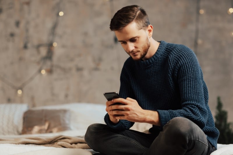 Man using his mobile phone while sitting on a bed at home