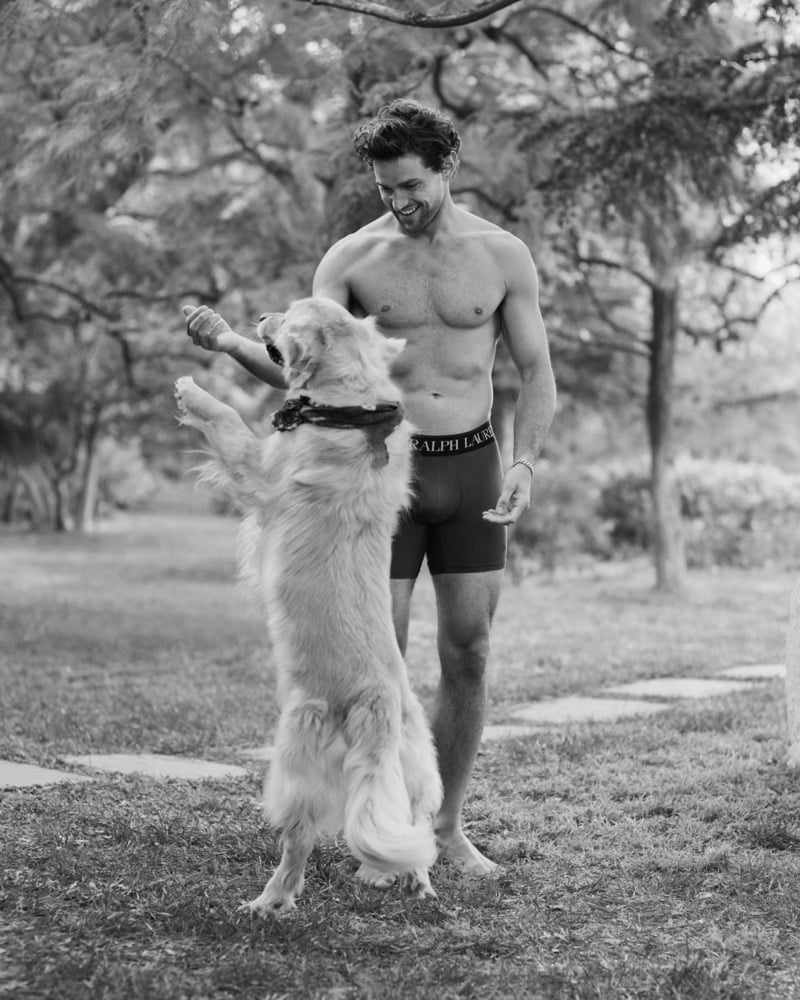 Black-and-white image of model Giacomo Cavalli playing with a golden retriever outdoors while wearing Polo Ralph Lauren boxer briefs