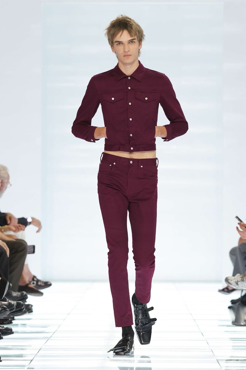 A Prada model walks the spring 2027 runway in a cropped burgundy denim jacket and matching slim burgundy jeans, finished with black multi-strap leather shoes