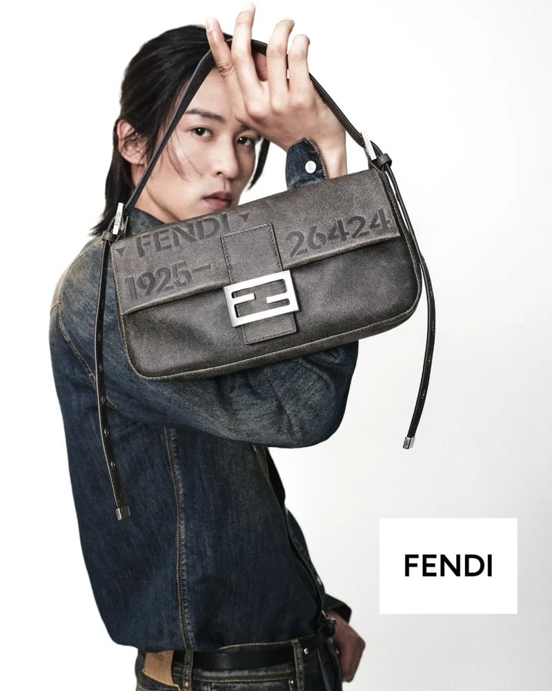 Ren Meguro holds the Fendi Baguette 26424 up in front of his denim shirt, arm raised by the strap, the bag's FENDI 1925-26424 embossing and silver FF clasp shown in profile