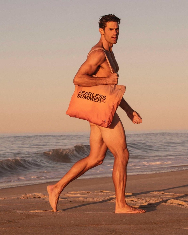 Chad White runs barefoot along the beach at sunset with the Fearless Summer tote bag slung over his shoulder