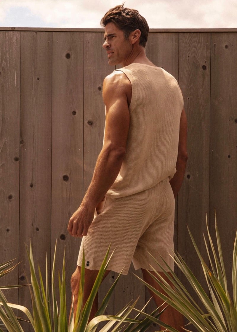 Chad White photographed from behind walking past a wood fence in a beige waffle-knit tank and matching shorts