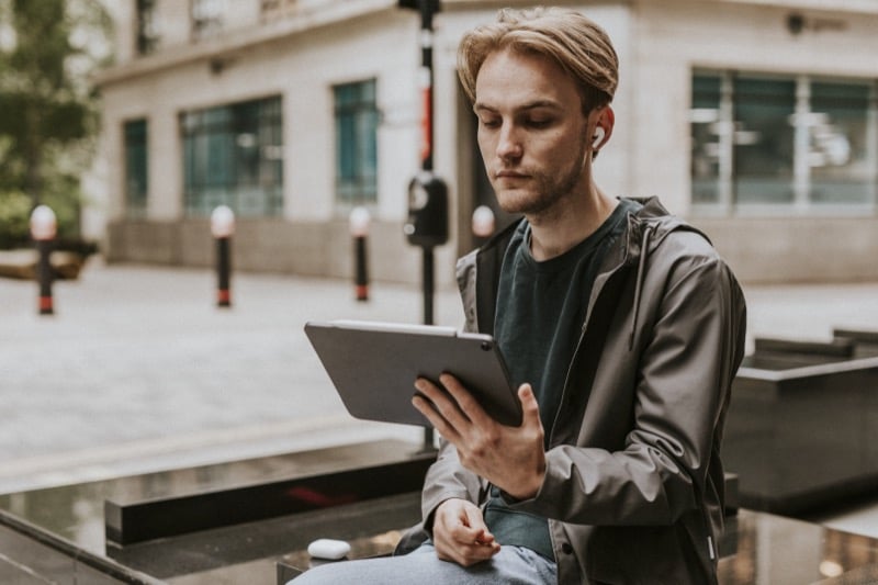 Man sitting outdoors in a city using a digital tablet