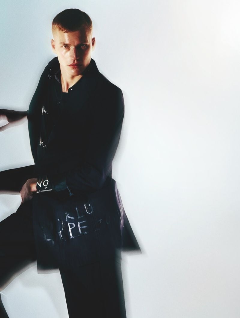 Timo Pan in a dark navy hand-lettered chalk-marker coat over a navy crewneck and matching cropped trousers, sleeves blurred mid-movement against a soft white backdrop