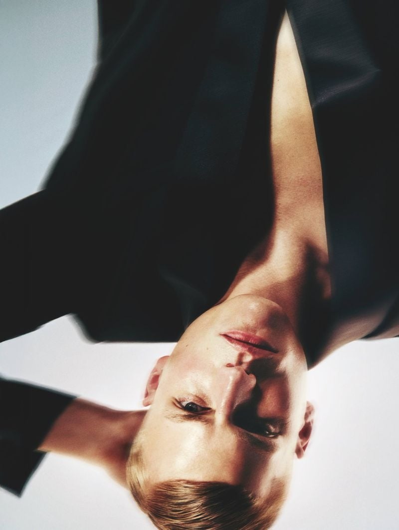Upside-down close-up portrait of Timo Pan with slick-back blond hair, photographed against a white backdrop with a dark blazer