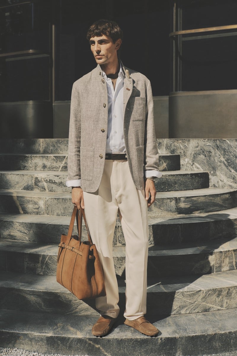 Model Joshua (Tomorrow is Another Day) in a sand linen single-breasted blazer over a pale blue button-down, paired with cream pleated trousers, tan suede Gommino loafers, and a tan suede tote