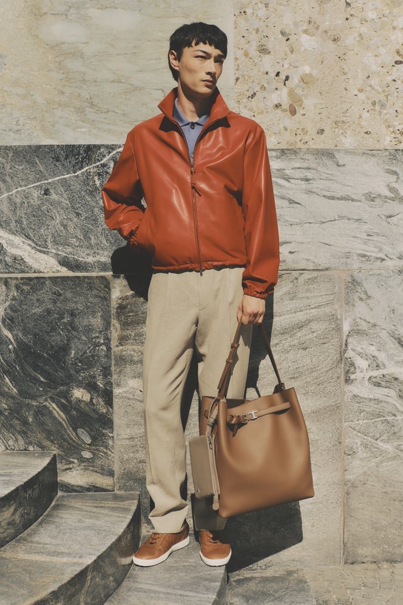 Model Pascal Thulin in a rust orange leather harrington jacket over a blue knit polo, paired with stone linen trousers, tan leather sneakers, and a camel leather tote
