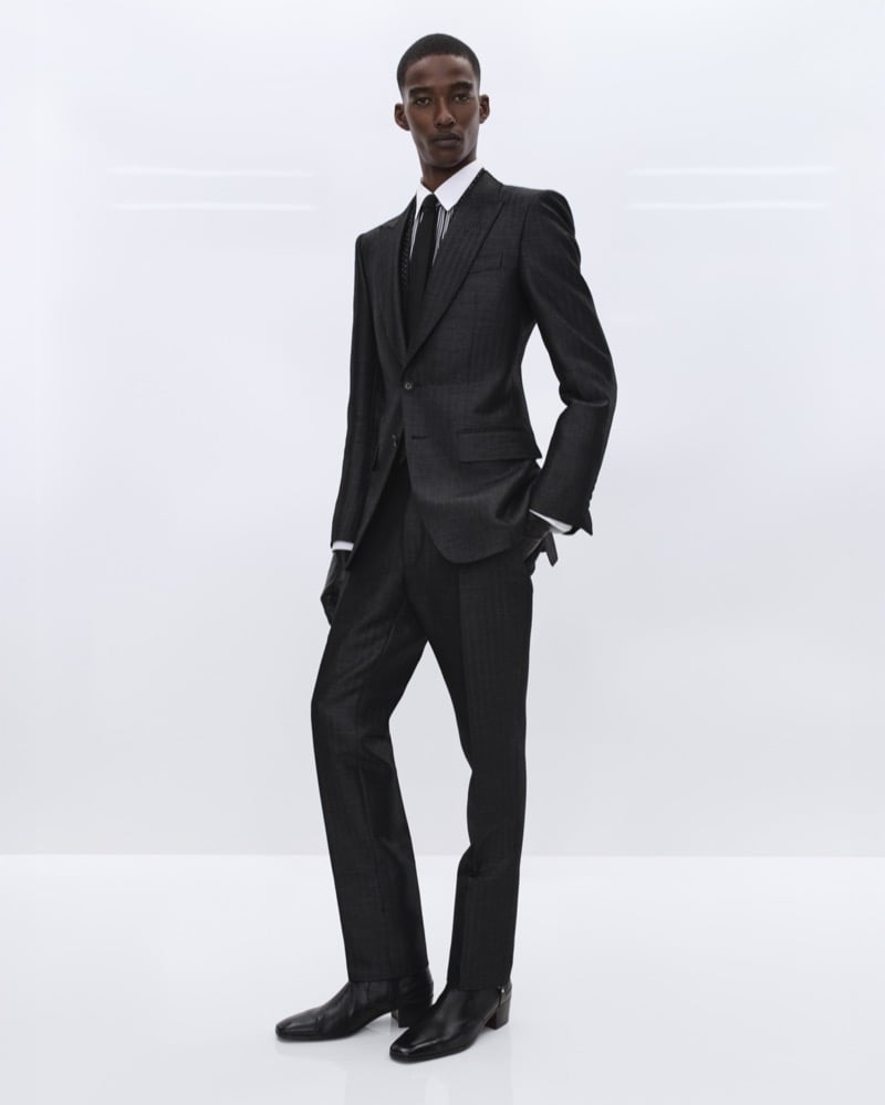 Samuel Elie wears a charcoal pinstripe single-breasted suit over a white shirt and black tie with a polka dot collar accent and black leather gloves