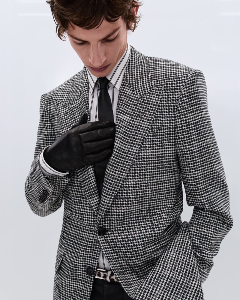 Elliot Belot wears a black and white houndstooth single-breasted jacket over a black and white striped shirt with a black tie and black leather gloves