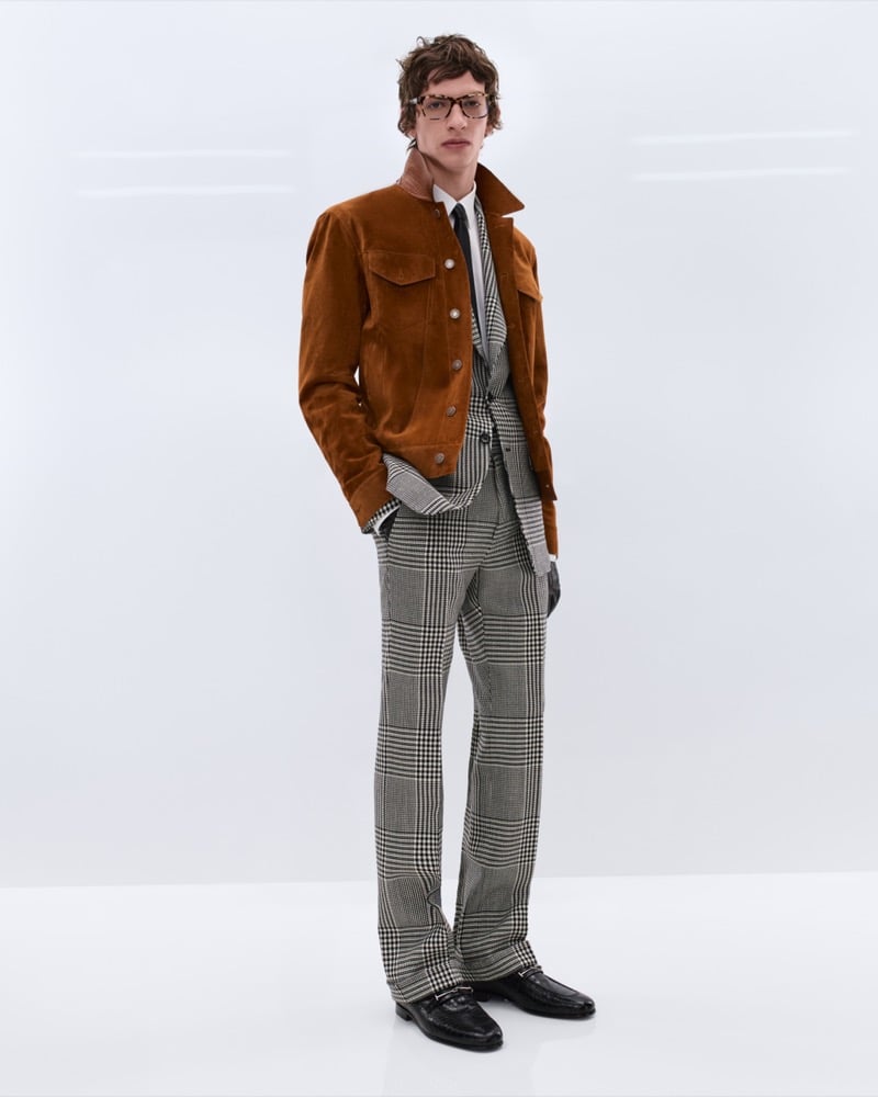 Elliot Belot wears tortoiseshell glasses and a tobacco suede trucker jacket over a Prince of Wales check suit with a black tie and black leather loafers