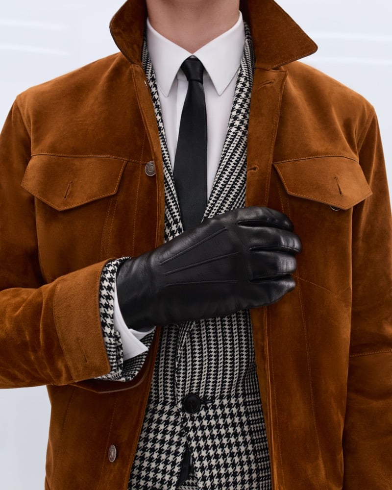 Elliot Belot wears a tobacco suede trucker jacket over a black and white houndstooth double-breasted blazer with a white shirt, black tie, and black leather gloves