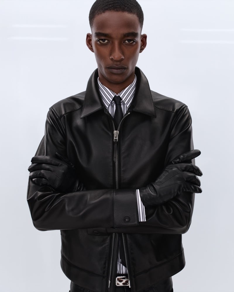 Samuel Elie wears a black leather zip-front jacket over a black and white striped shirt with long black leather opera gloves