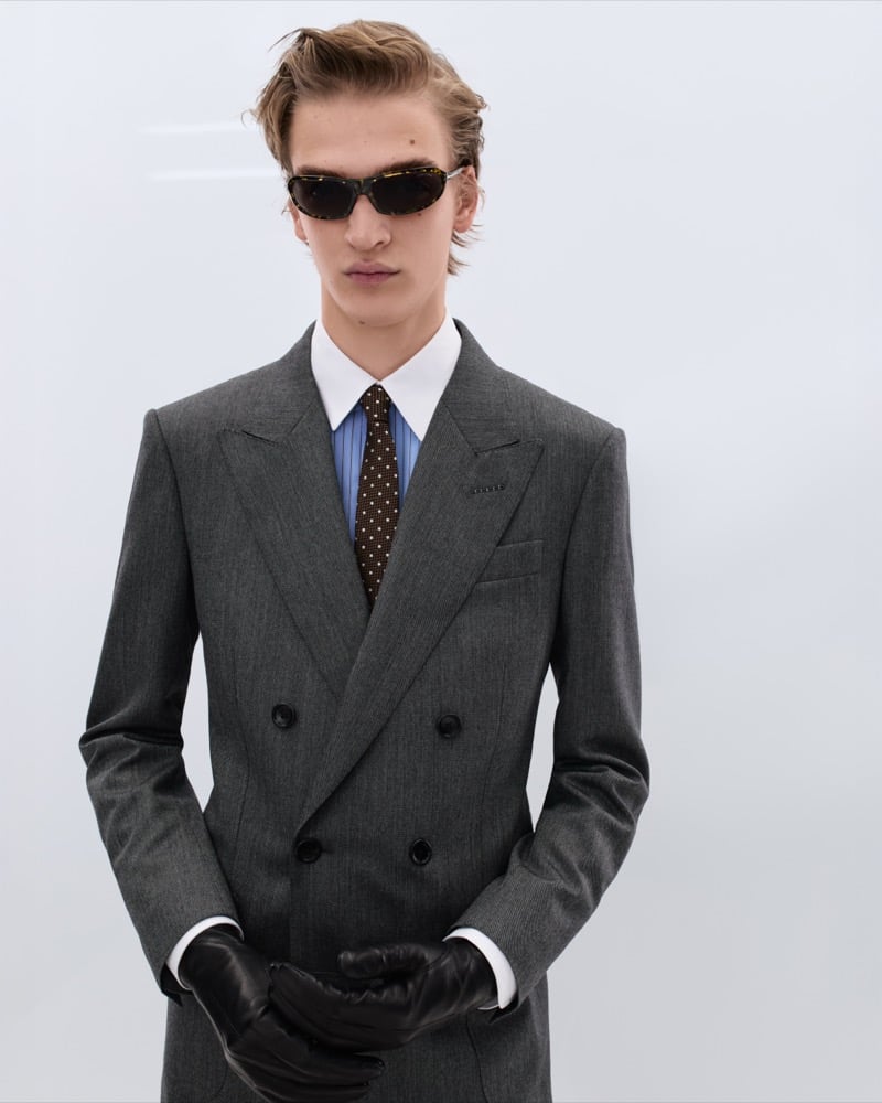 Dario Tonin wears tortoiseshell sunglasses with a grey double-breasted flannel suit over a blue striped shirt and brown polka dot tie with black leather gloves