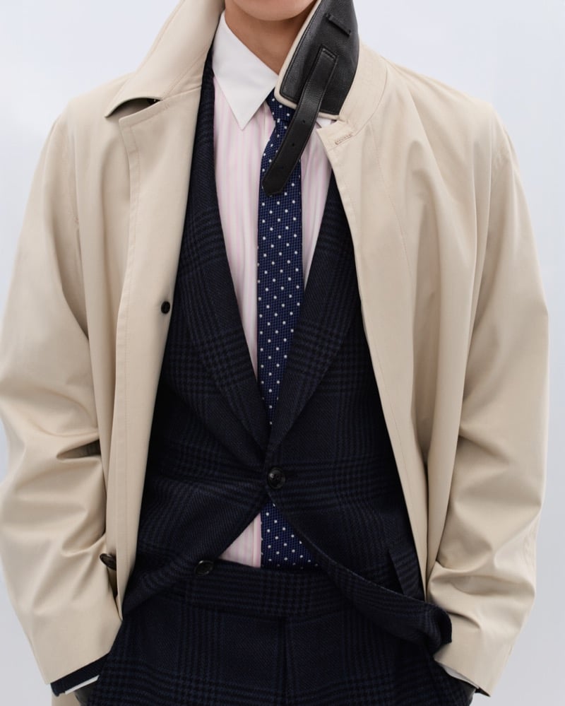 Cirillo wears a beige trench coat over a navy Prince of Wales check waistcoat and pink striped shirt with a navy polka dot tie