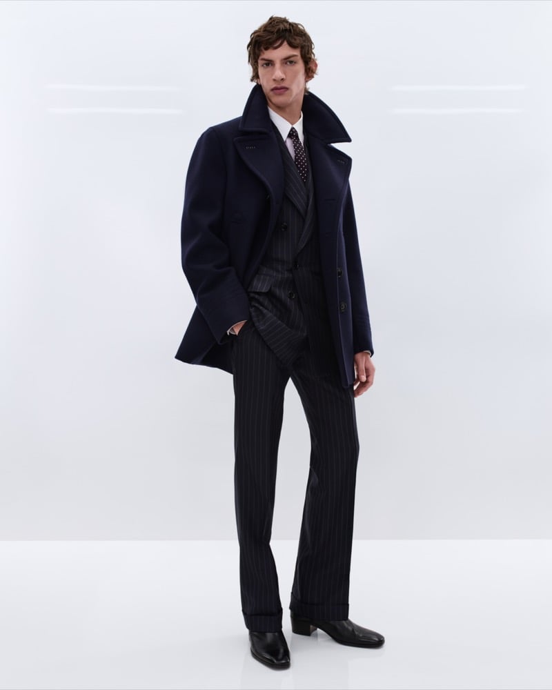 Elliot Belot wears a navy wool peacoat over a charcoal pinstripe double-breasted suit with a white shirt and burgundy polka dot tie