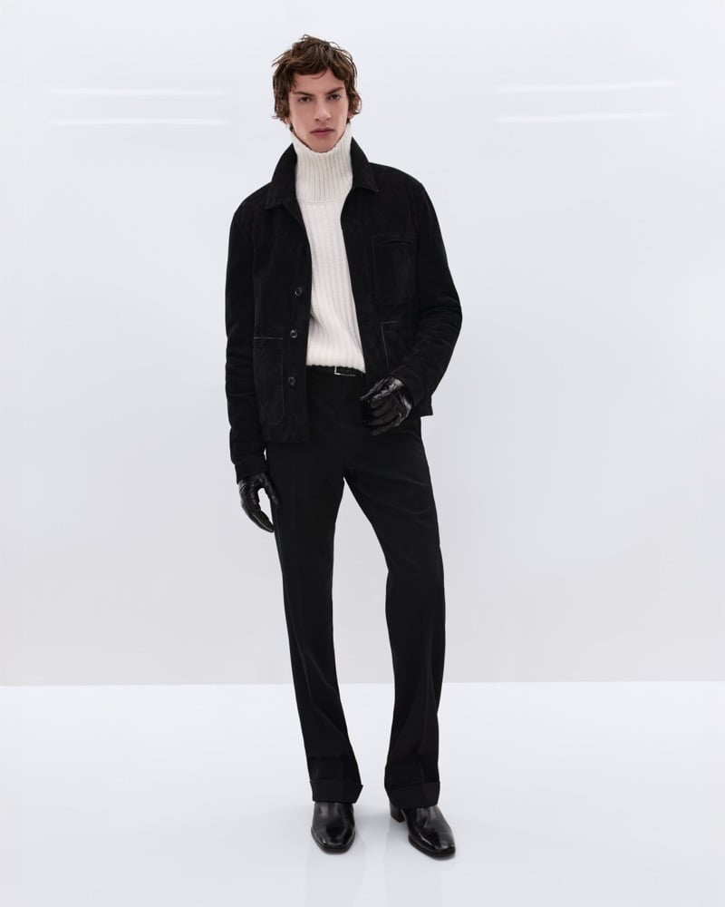 Elliot Belot wears a black suede shirt jacket over a cream ribbed cashmere turtleneck with black wool trousers and black leather gloves and Chelsea boots