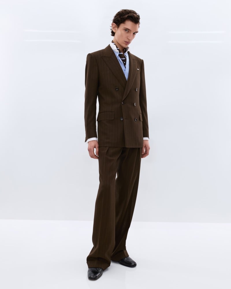 Cirillo wears a brown chalk stripe double-breasted suit over a blue striped shirt with a brown patterned silk scarf knotted at the neck