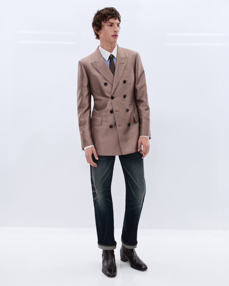 Elliot Belot wears a camel double-breasted blazer over a white shirt and brown polka dot tie with washed indigo straight-leg jeans and brown leather Chelsea boots