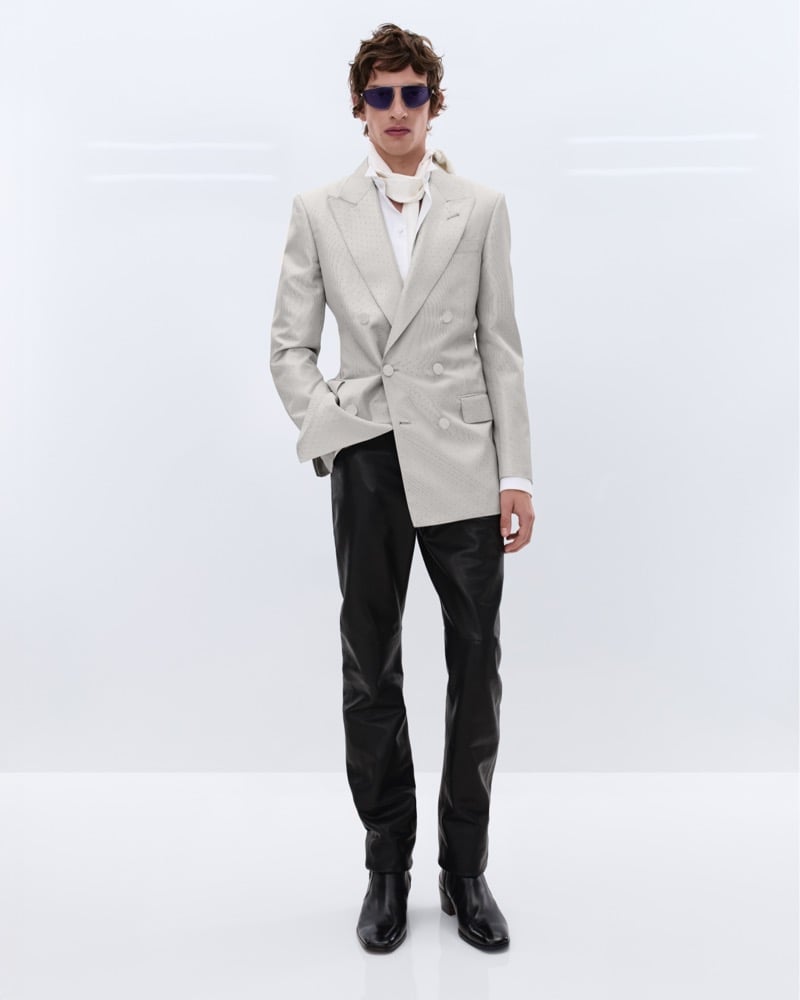 Elliot Belot wears blue-tinted sunglasses and a cream textured double-breasted blazer over a white shirt with an ivory silk scarf and black leather trousers