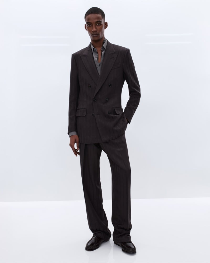Samuel Elie wears a dark brown pinstripe double-breasted suit over an open grey silk shirt with a beaded chain necklace and brown leather loafers