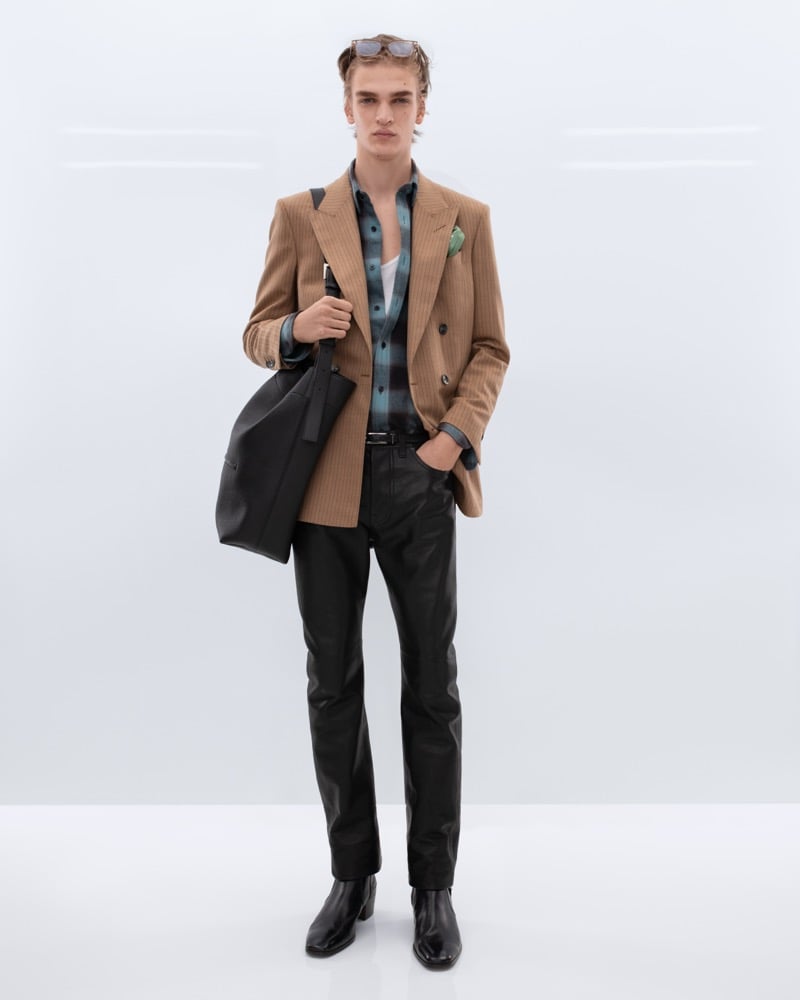 Dario Tonin wears tortoiseshell sunglasses pushed up on his head and a camel pinstripe double-breasted blazer over a teal ombre flannel shirt and white tank with black leather trousers, carrying a black leather tote