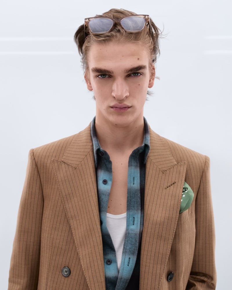 Dario Tonin wears tortoiseshell sunglasses pushed up on his head with a camel pinstripe double-breasted blazer over a teal ombre flannel shirt, white tank, and green silk pocket square