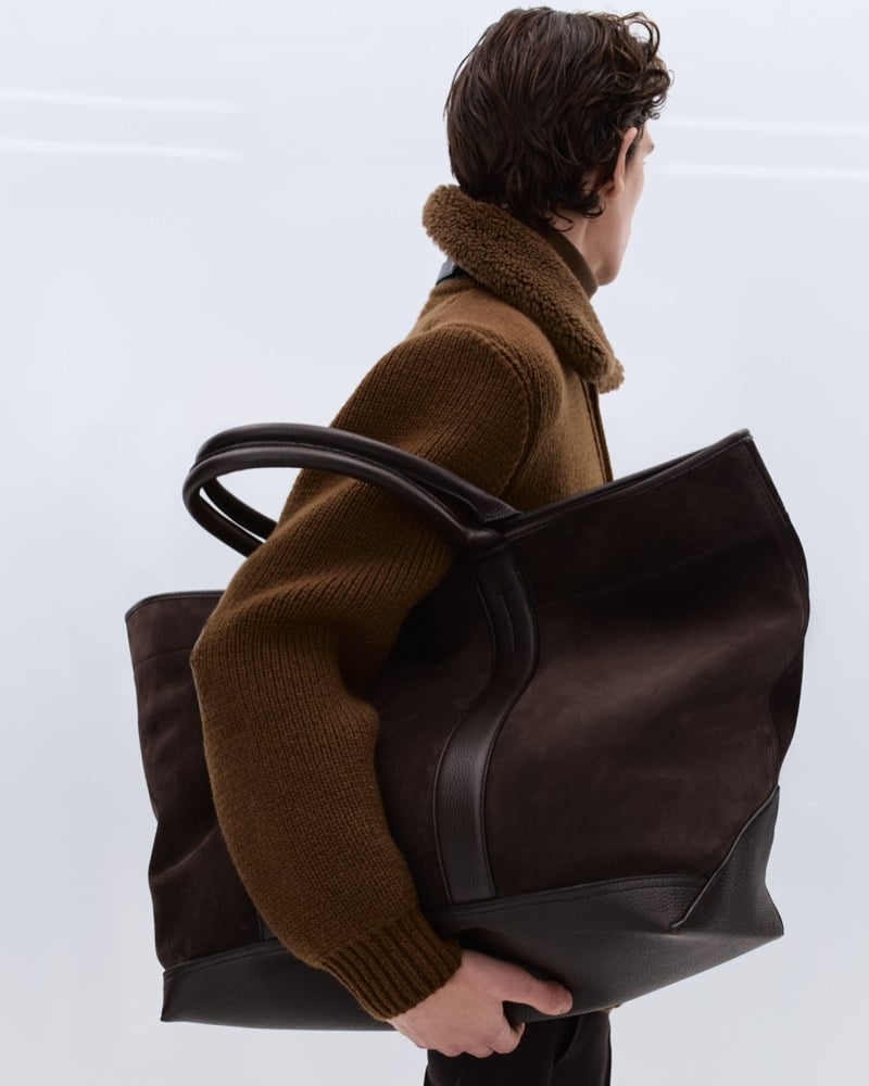 Cirillo wears a tobacco ribbed wool sweater with a brown shearling collar leather jacket, carrying a large dark brown suede and leather Tom Ford tote