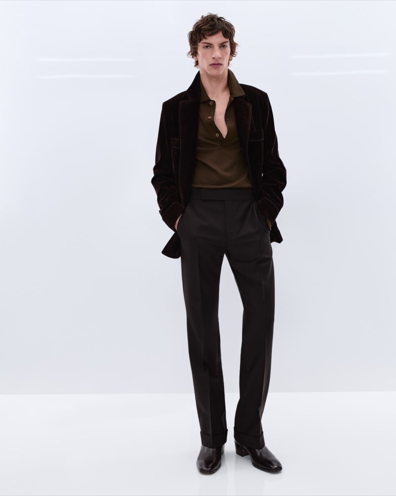 Elliot Belot wears a dark brown velvet shirt jacket over an olive polo with charcoal wool trousers and dark brown leather Chelsea boots