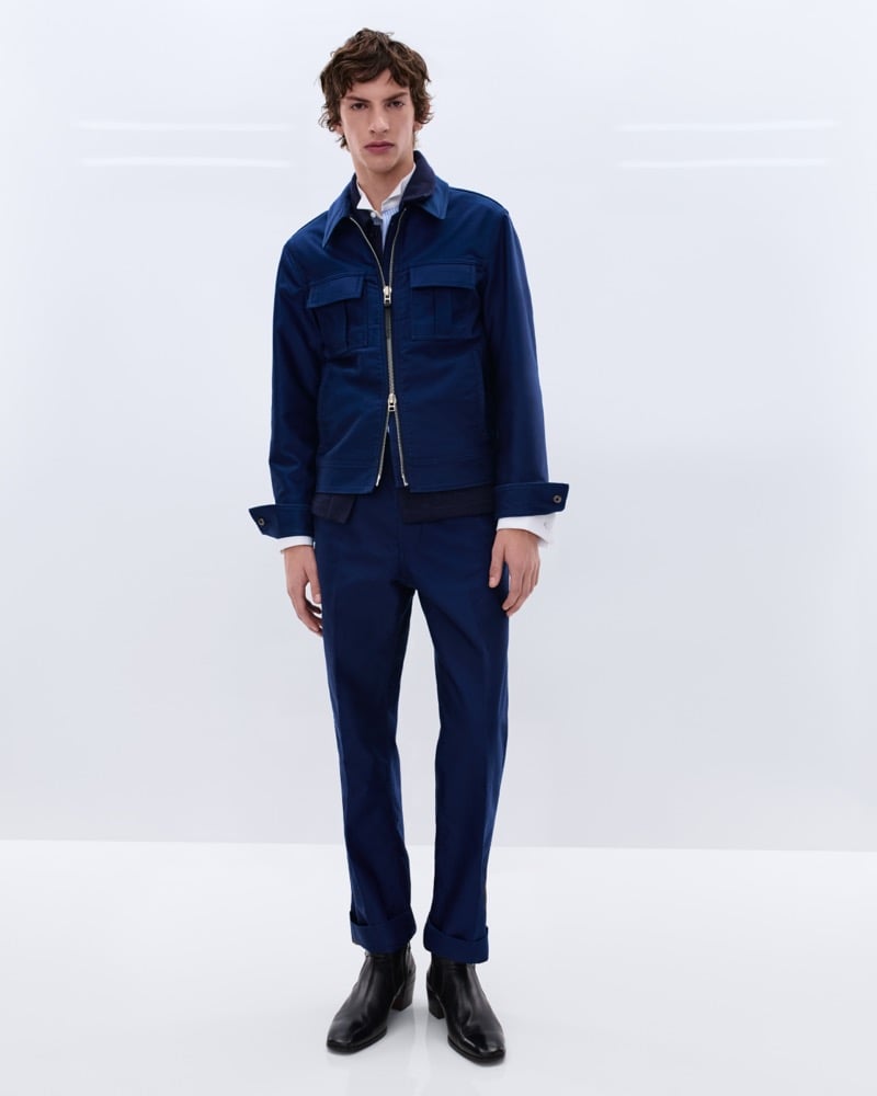 Elliot Belot wears a royal blue cotton zip-front workwear jacket over a white shirt with matching royal blue trousers and black leather Chelsea boots