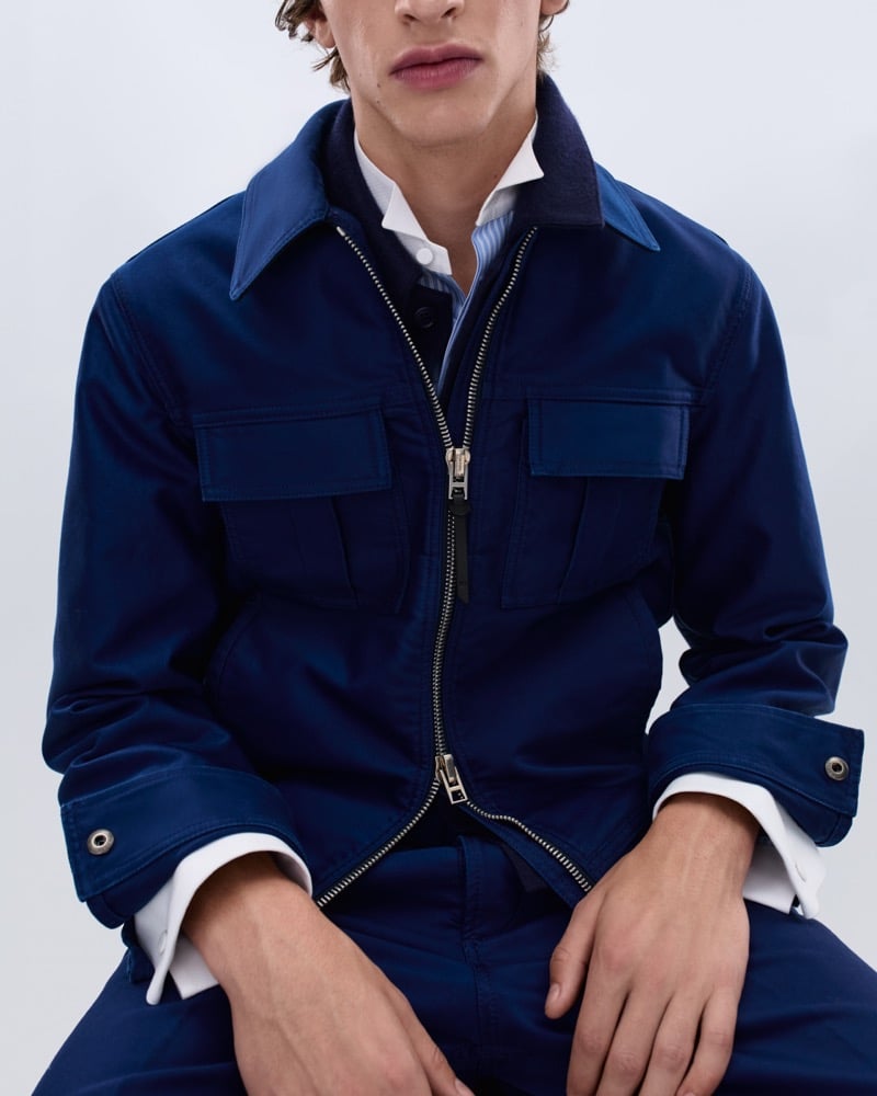 Elliot Belot wears a royal blue cotton workwear jacket with utility chest pockets over a white shirt and pale blue striped layer
