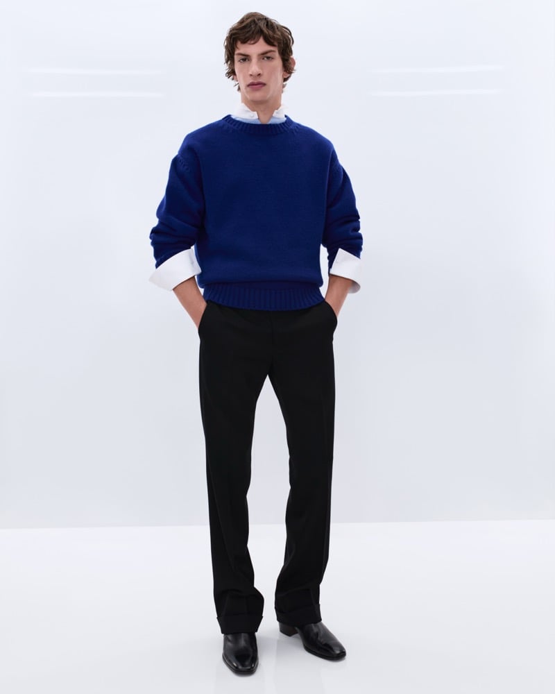 Elliot Belot wears an oversized cobalt blue wool crewneck sweater over a white shirt with black wool trousers and black leather Chelsea boots