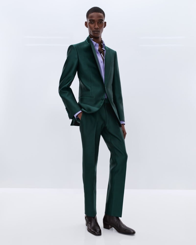 Samuel Elie wears a forest green sharkskin single-breasted suit over a lavender shirt with a printed silk scarf at the neck and brown leather Chelsea boots
