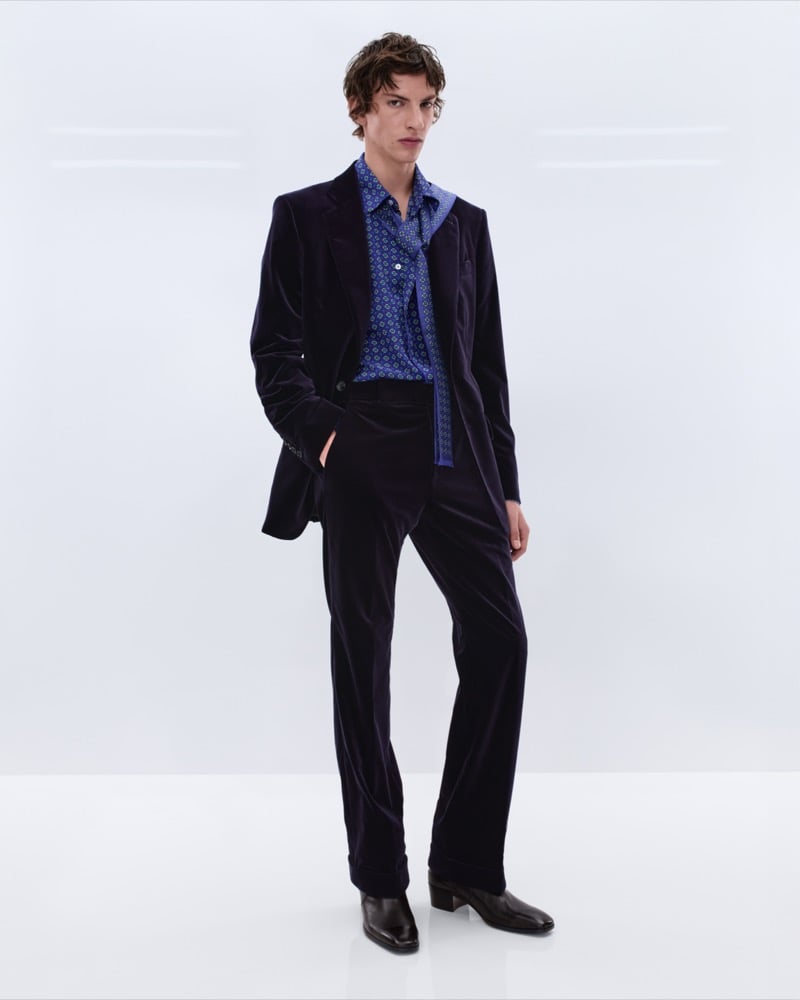 Elliot Belot wears a midnight blue velvet single-breasted suit over a blue medallion print silk shirt with a matching scarf and brown leather Chelsea boots