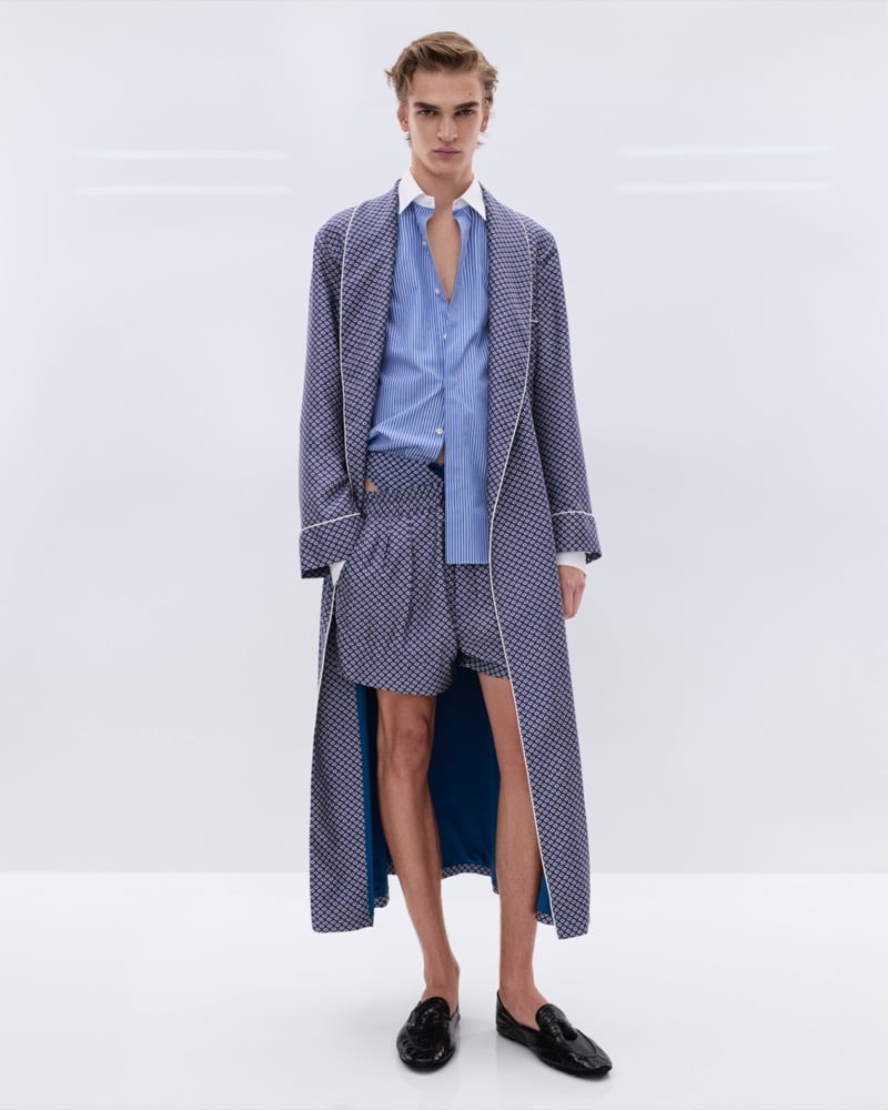 Dario Tonin wears a blue geometric print silk pajama robe over a blue and white striped shirt with matching geometric print boxer shorts and black leather woven loafers
