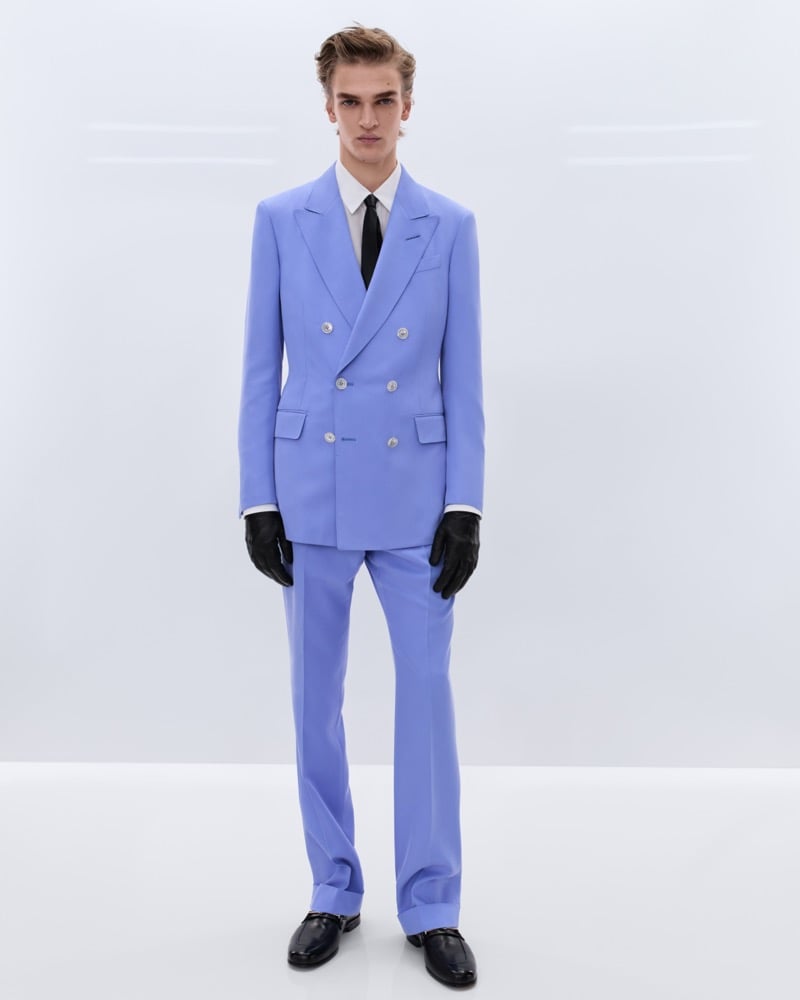 Dario Tonin wears a periwinkle blue double-breasted suit over a white shirt and black tie with long black leather gloves and black leather penny loafers